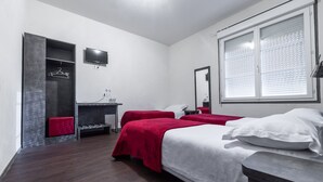 Een hotelkamer met twee bedden, een televisie, een spiegel, een raam met zonwering, een kledingkast en een klein bureau met stoel.