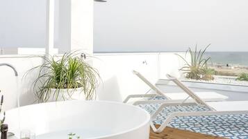 Ein Balkon mit einer weißen Badewanne, Liegestühlen und Blick auf den Strand.