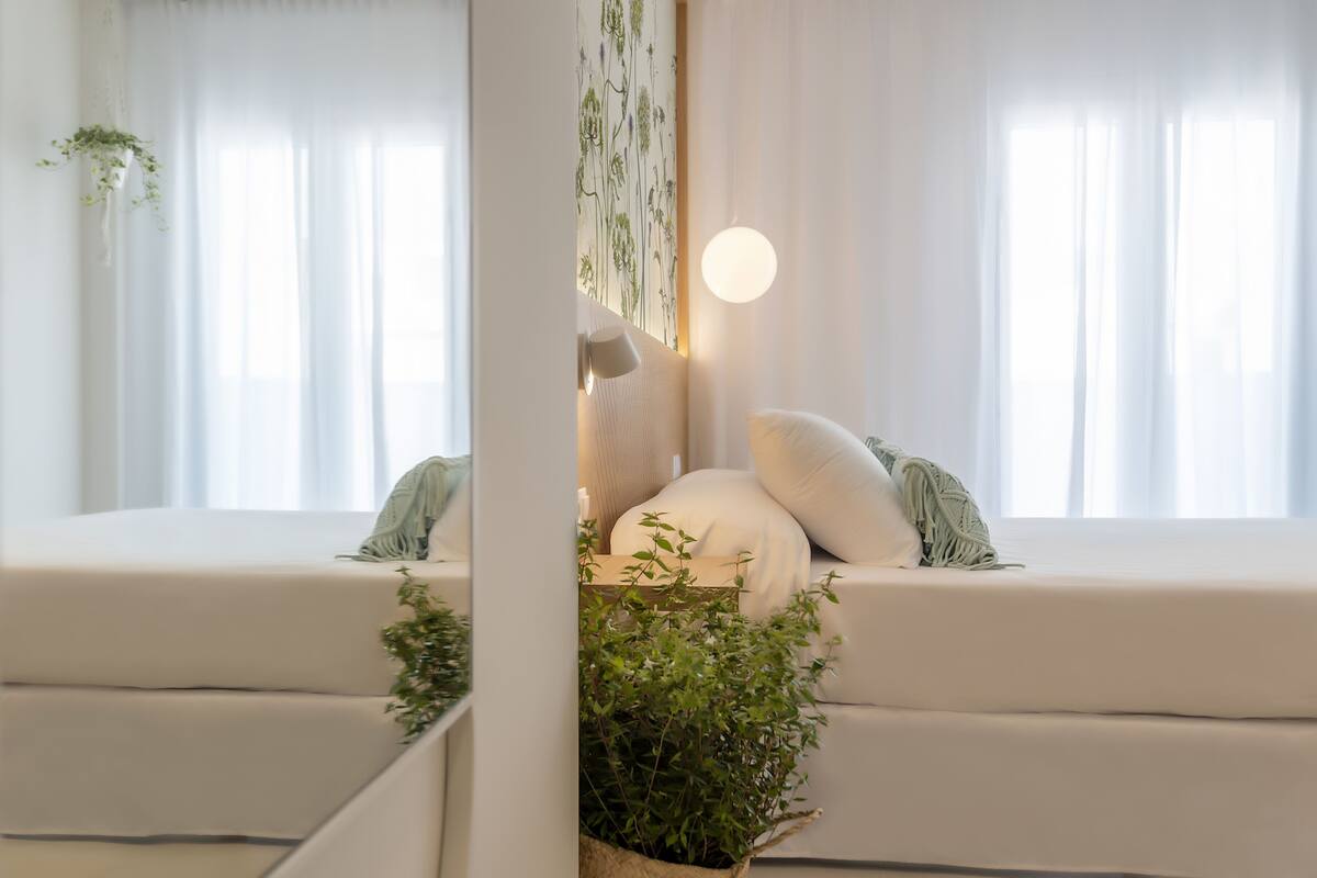 Une pièce moderne et bien éclairée, dotée d’une grande fenêtre, d’un canapé avec des coussins et d’une plante suspendue.