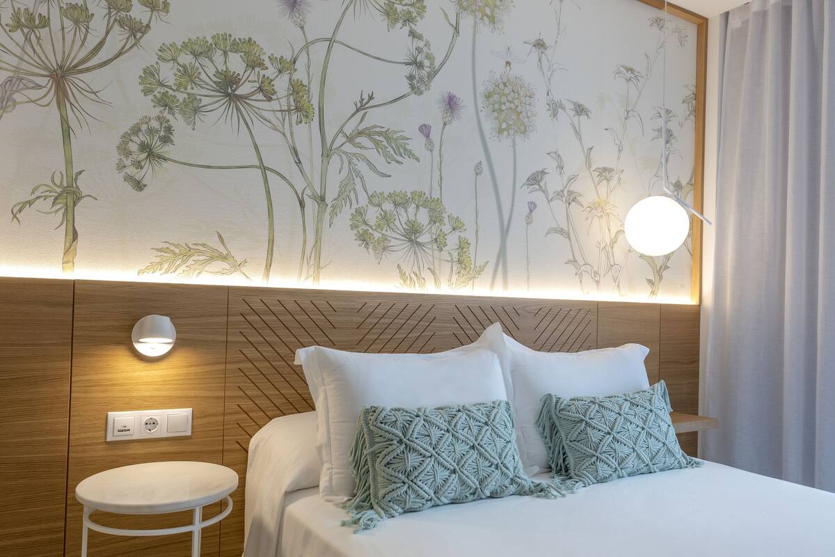 Une chambre d’hôtel avec un lit, une petite table ronde, une lampe fixée au mur et une prise de courant.