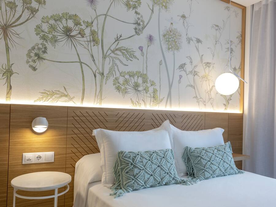 Een hotelkamer met een bed, een klein rond tafeltje, een wandlamp en een stopcontact.