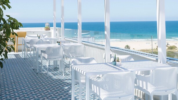 Een overdekt terras met witte stoelen en tafels, met uitzicht op de oceaan.
