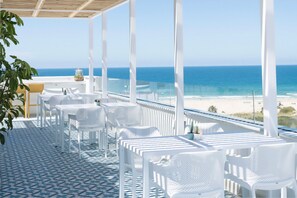 Een overdekt terras met witte stoelen en tafels, met uitzicht op de oceaan.