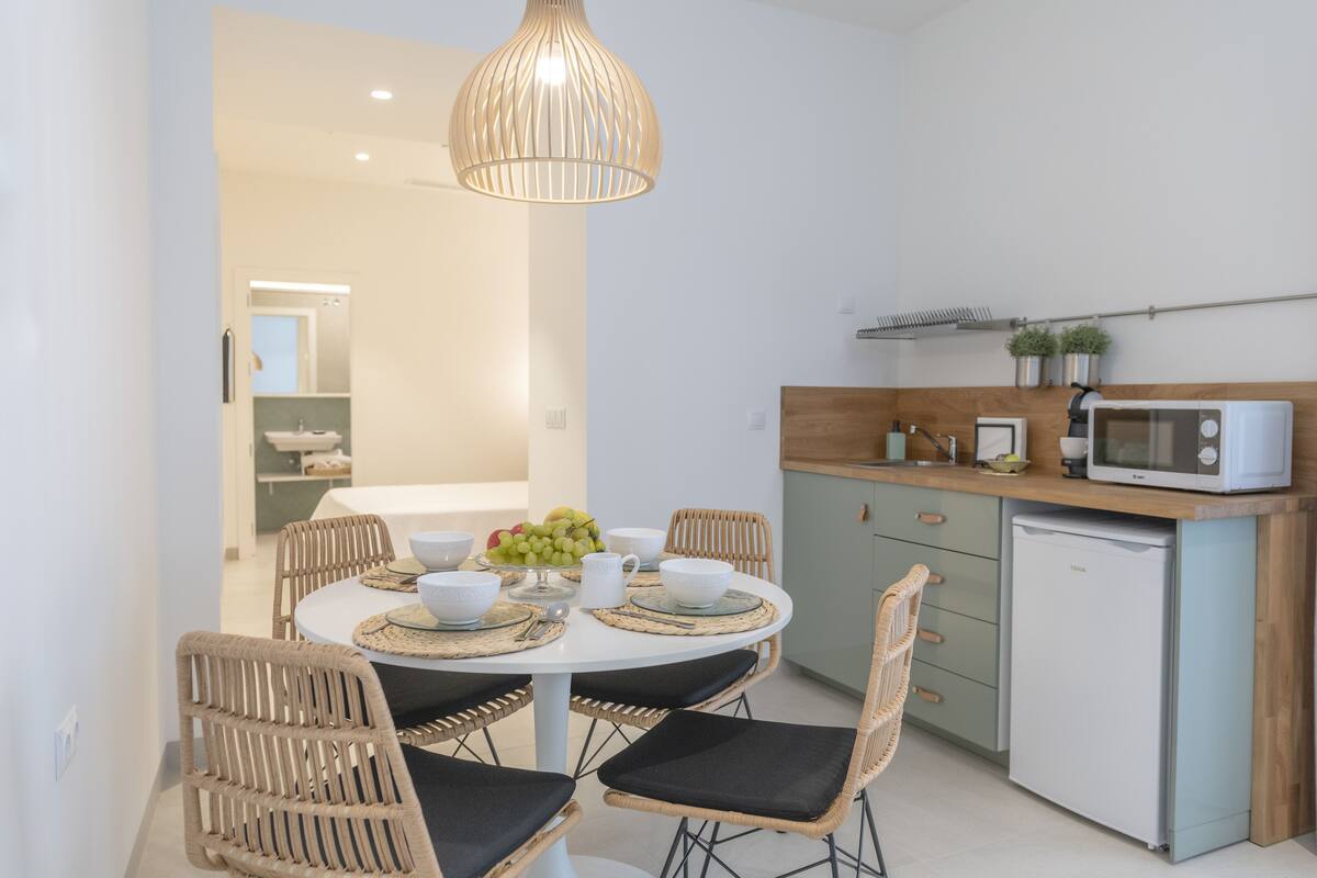 Une cuisine compacte équipée d’un four à micro-ondes, d’un petit réfrigérateur et d’un coin repas avec des chaises en osier et une table blanche.
