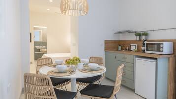 A compact kitchen with a microwave, a small refrigerator, and a dining area with wicker chairs and a white table.