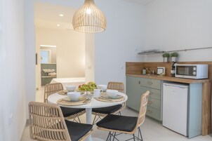 A compact kitchen with a microwave, a small refrigerator, and a dining area with wicker chairs and a white table.
