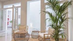 Een moderne lobby met een grote glazen deur, rieten meubels en een potplant.