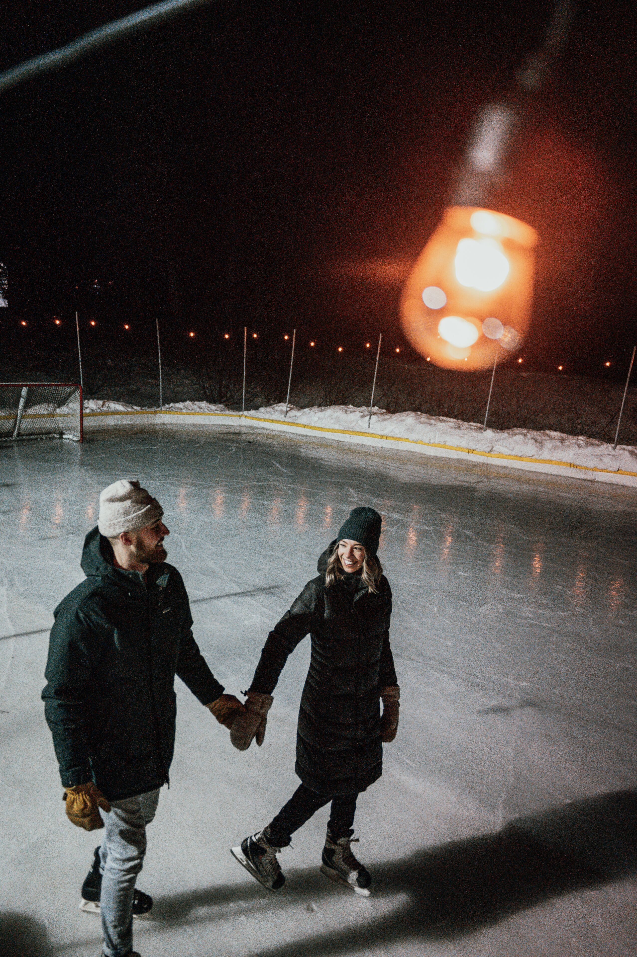 Two people holding hands on an ice rink at night.