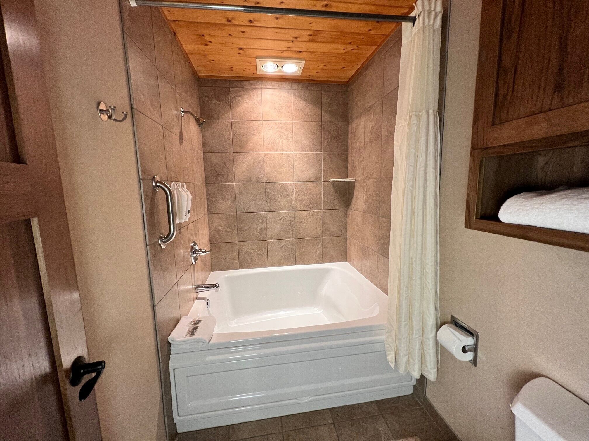 Une salle de bain avec une baignoire, un plafond en bois et des murs carrelés.
