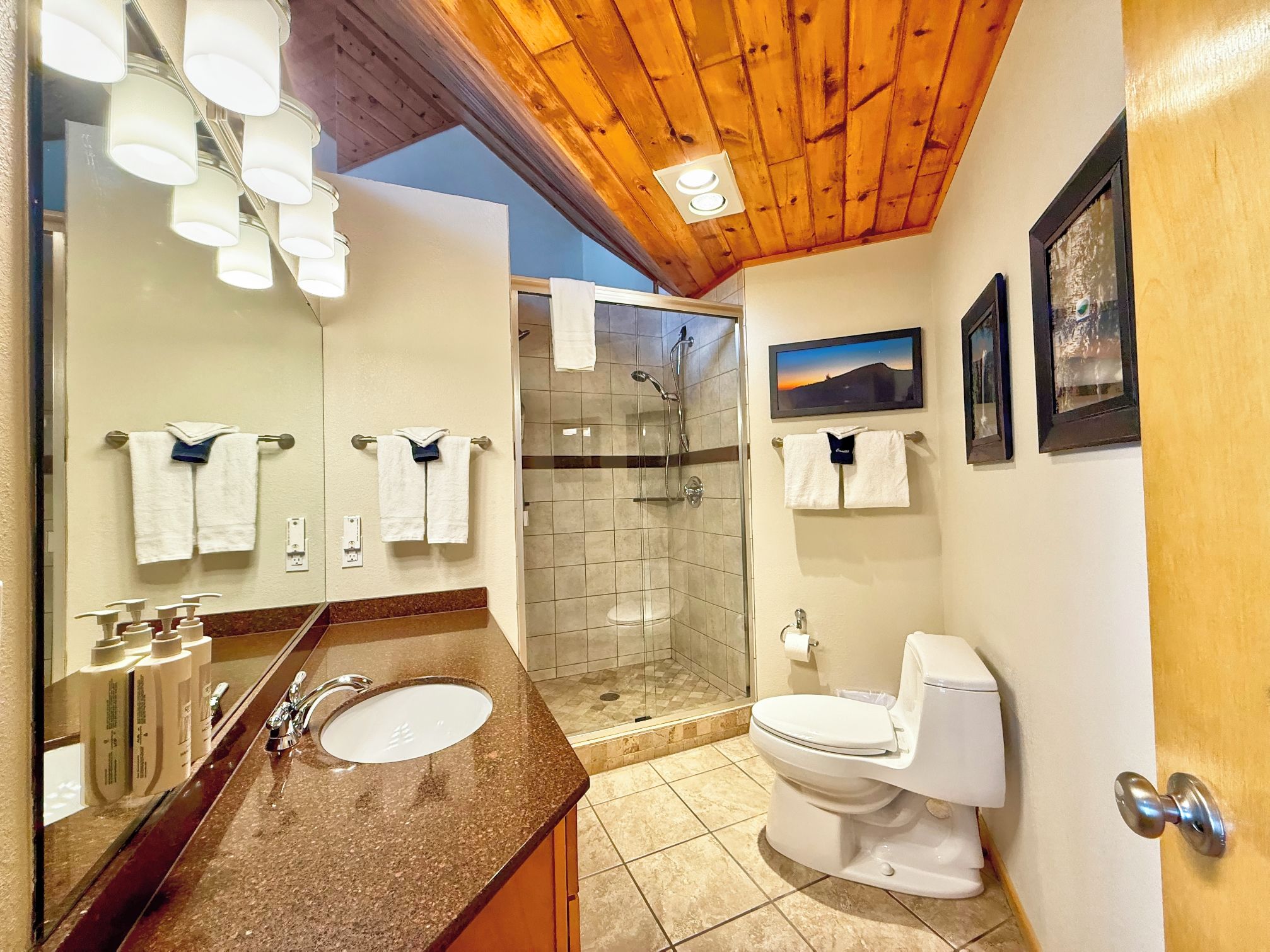 Une salle de bain équipée d’une douche, de toilettes et d’un lavabo, avec des serviettes suspendues à des crochets et un miroir au-dessus du lavabo.