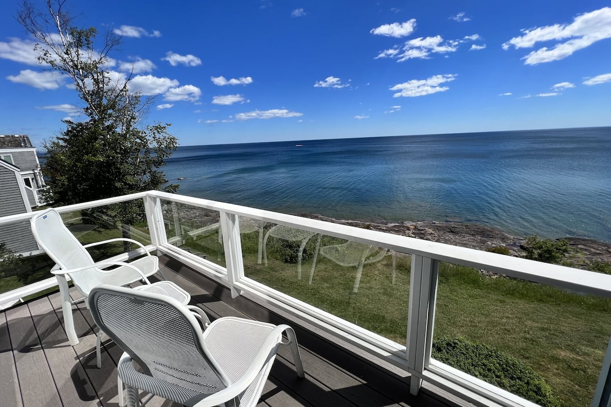 A deck with white metal chairs and a white railing overlooking a body of water.