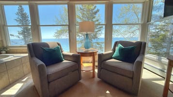 A sunroom with two armchairs, a small table with a lamp, and a view of the sea through large windows.