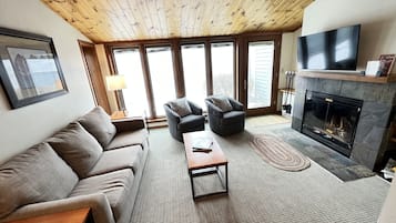 Una sala de estar acogedora con techo de madera, chimenea, sofá, sillón y televisor.