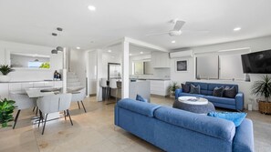 A modern living room with a blue sofa, a dining area with a glass table, and a kitchen with white cabinets. - Taralla 1 (Noosa Heads)