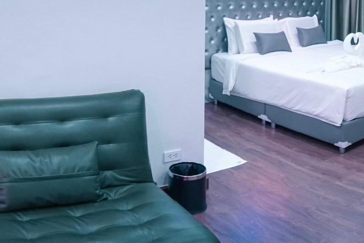 A modern hotel room with a green upholstered sofa, a grey upholstered bed with white bedding, and a wooden floor.
