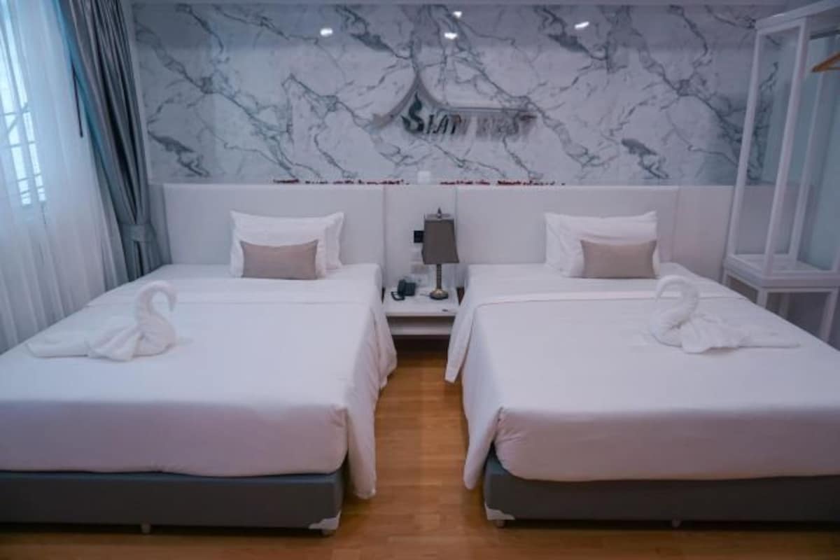 Een hotelkamer met twee bedden, een marmeren wand en een nachtkastje met een lamp.