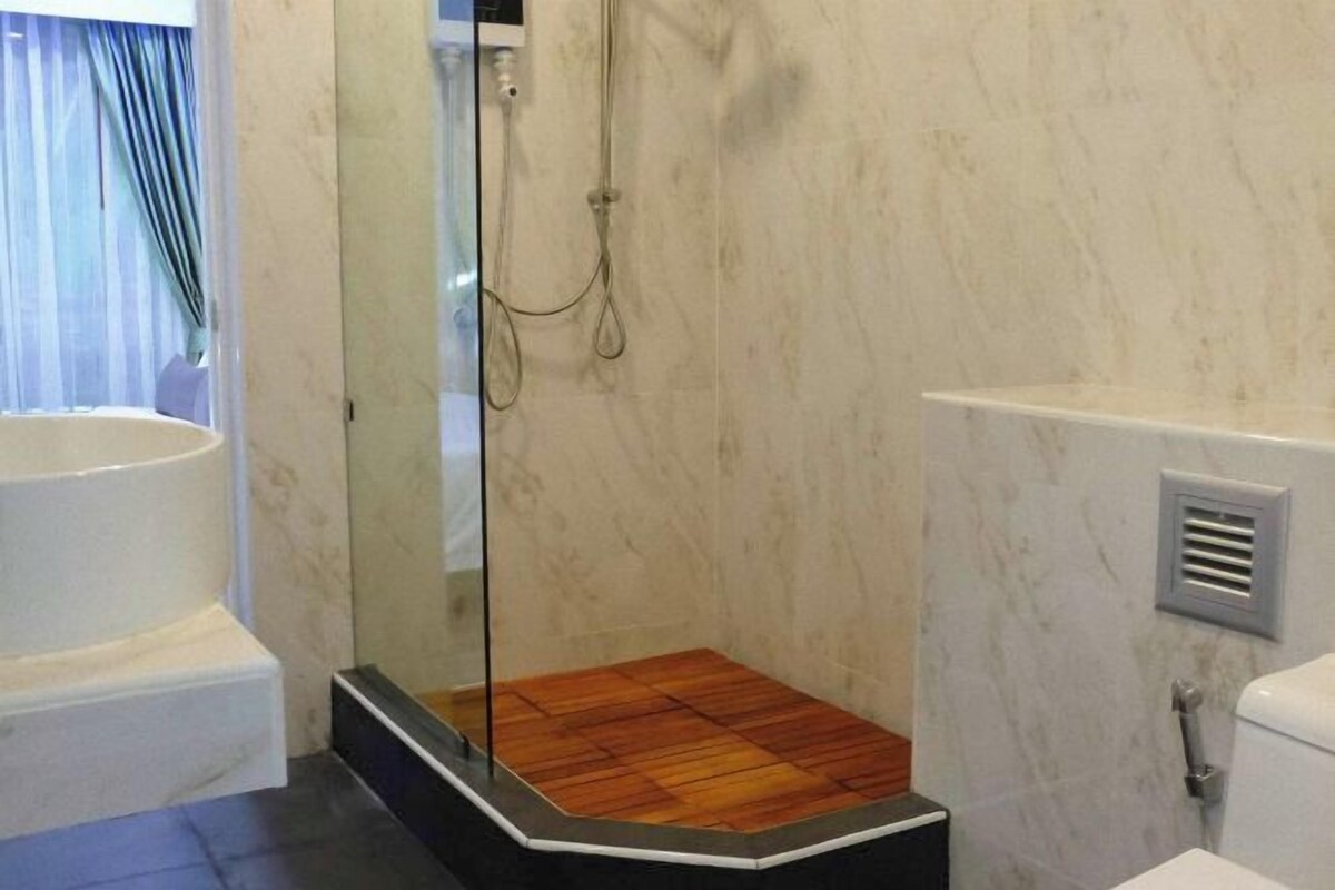 Een badkamer met een houten doucheplatform, een bad en een marmeren wand.