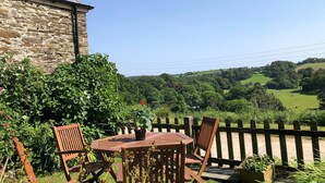 A stone building with a wooden table and chairs in a garden. - Tregarland Farm (Looe)
