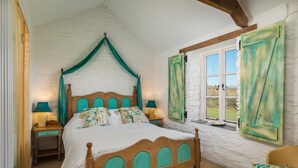 A bedroom with a wooden bed, green curtains, and a window with a view of the outdoors. - Tregarland Farm (Looe)