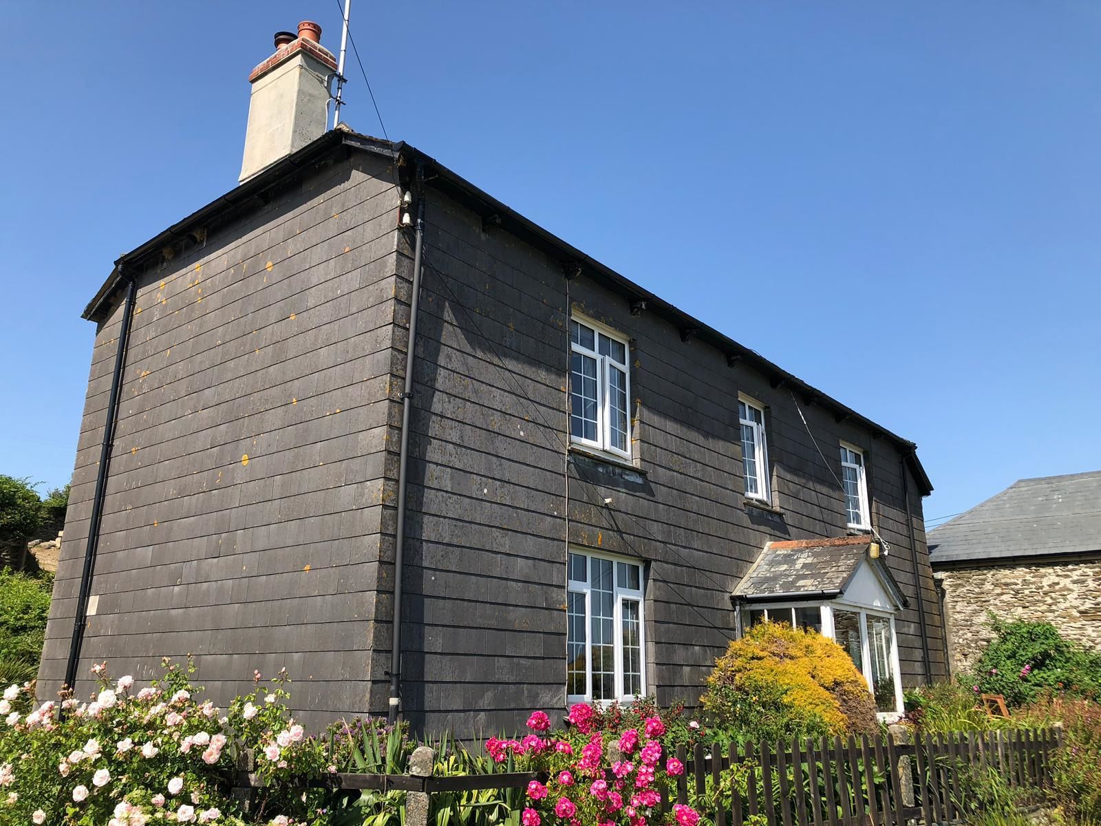 A two-story house with a dark wooden exterior, a chimney, and a stone wall on the right side.