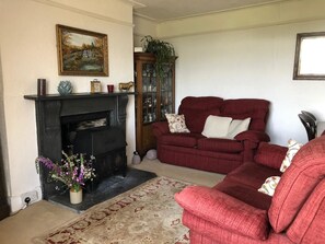 A living room with a fireplace, a red sofa, and a patterned rug. - Tregarland Farm (Looe)