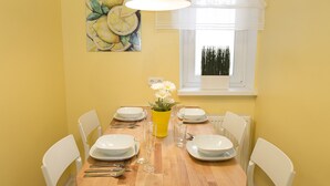 A dining area with a wooden table set for four, white chairs, a yellow vase with flowers, and a painting of lemons on the wall. - Ferienwohnung Raab (Nuremberg)