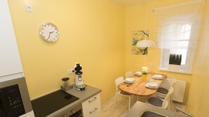 A compact kitchen with a stove, oven, and sink. There is a dining table with chairs and a clock on the wall. - Ferienwohnung Raab (Nuremberg)