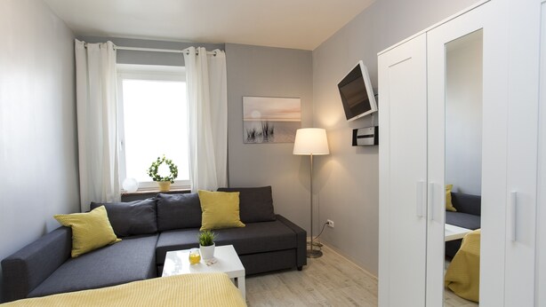 A modern room with a grey sofa, a small white table, a floor lamp, and a wardrobe. - Ferienwohnung Raab (Nuremberg)