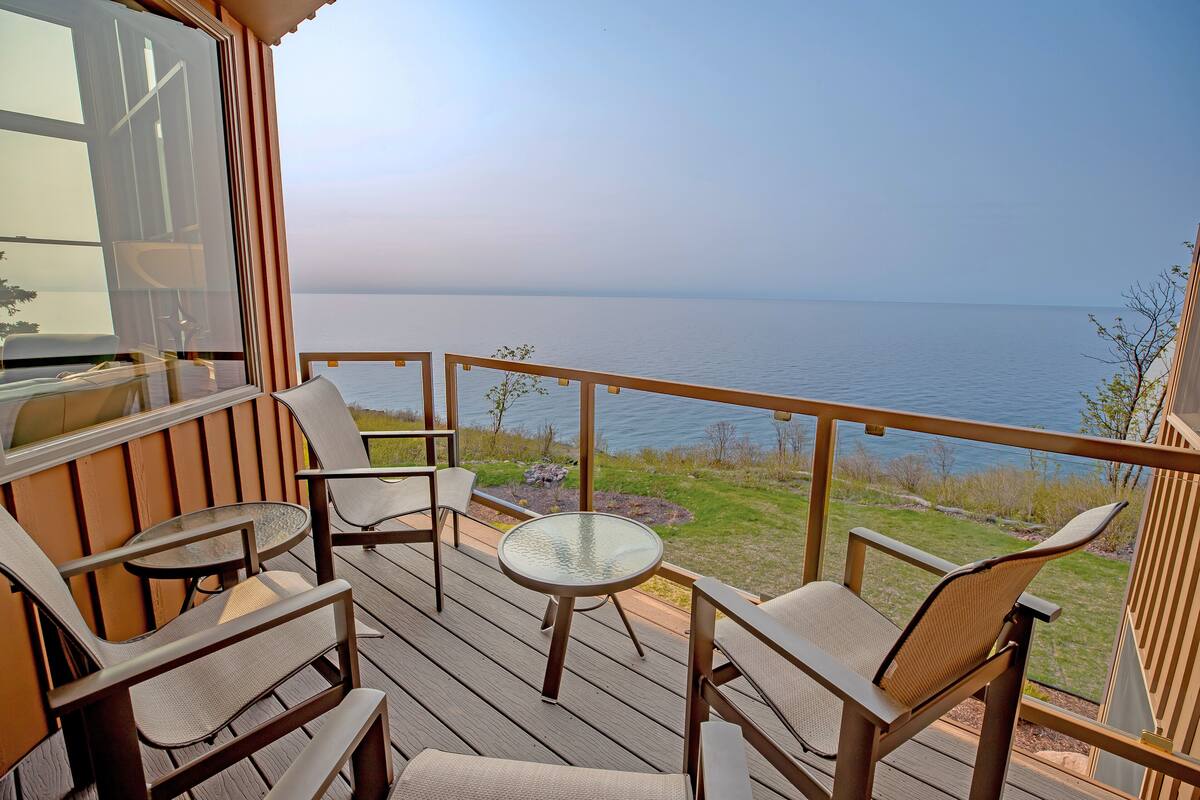 A deck with outdoor furniture, a glass table, and a view of the water.