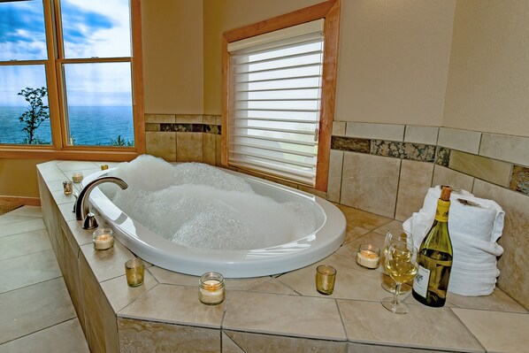 A bathroom with a large bathtub, candles, and a bottle of wine.