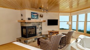 A modern living room with a fireplace, comfortable seating, a large window with a view, and a flat-screen TV mounted on the wall. - Surfside on Lake Superior (Tofte)