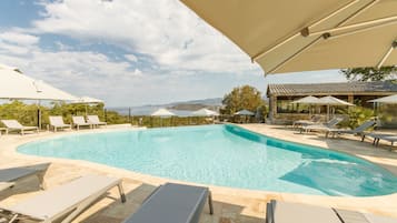 Relax by the rectangular pool surrounded by lounge chairs and umbrellas, with a view of the nearby building and distant mountains.