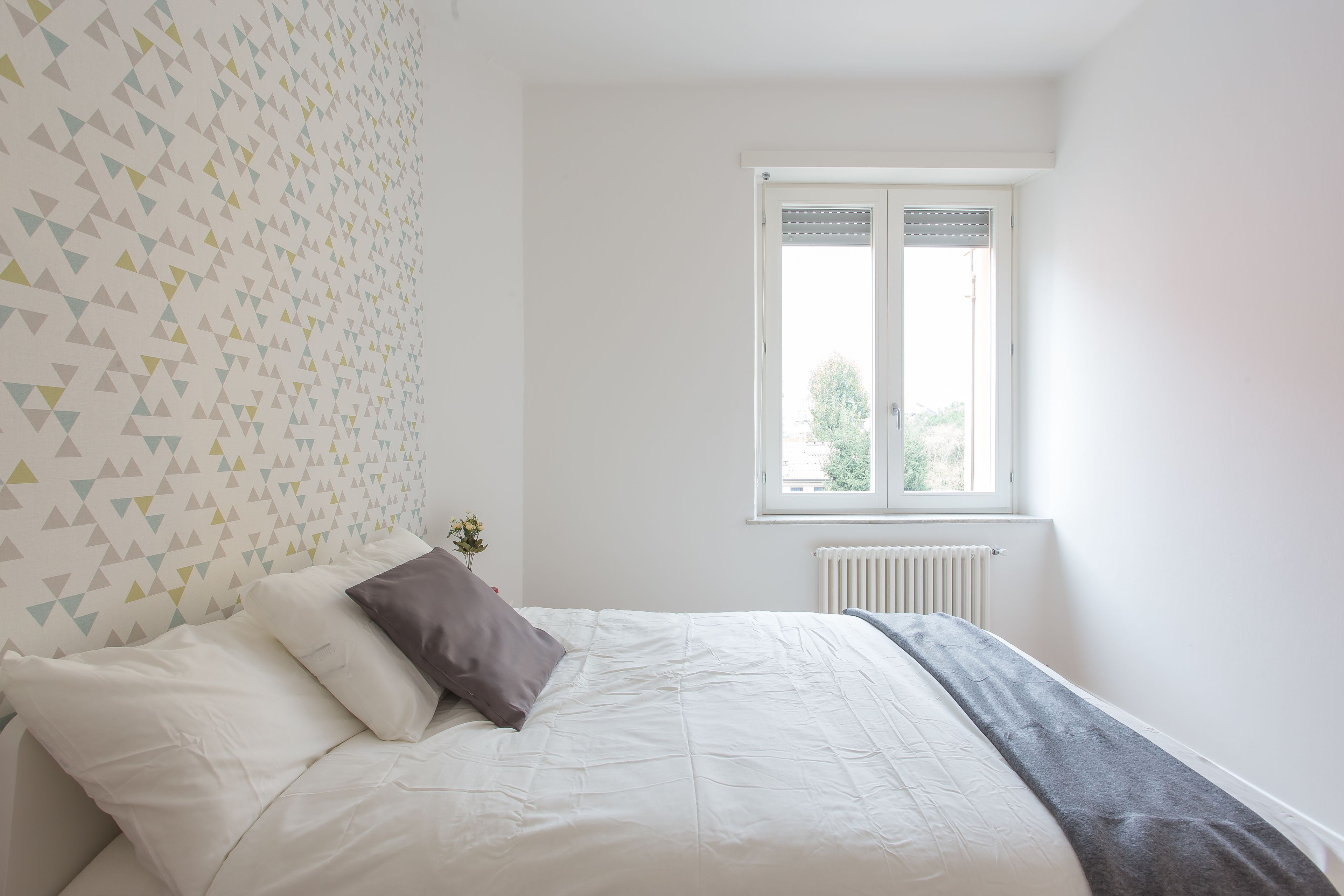 A bedroom with a bed, pillows, a radiator, and a window.