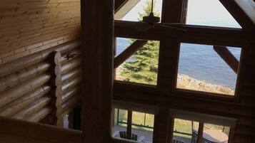 A log cabin interior with a large window overlooking a deck and water.