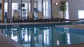 An indoor swimming pool with lounge chairs and exercise equipment.