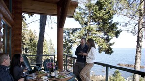 A wooden deck with a table set for dining, overlooking a body of water and surrounded by trees. - Temperance Landing on Lake Superior (Schroeder)
