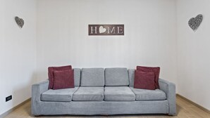 A grey sofa with three cushions, two red and one grey, in a room with a 'HOME' sign on the wall. - Cassola - Via Loria 12 (Cassola)