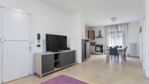 A modern living space with a flat-screen TV on a wooden console, a dining area with a table and chairs, and a kitchen with a stove and cabinets. - Cassola - Via Loria 12 (Cassola)