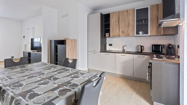 A compact kitchen with modern appliances, a dining area with a patterned tablecloth, and a small seating area. - Cassola - Via Loria 12 (Cassola)