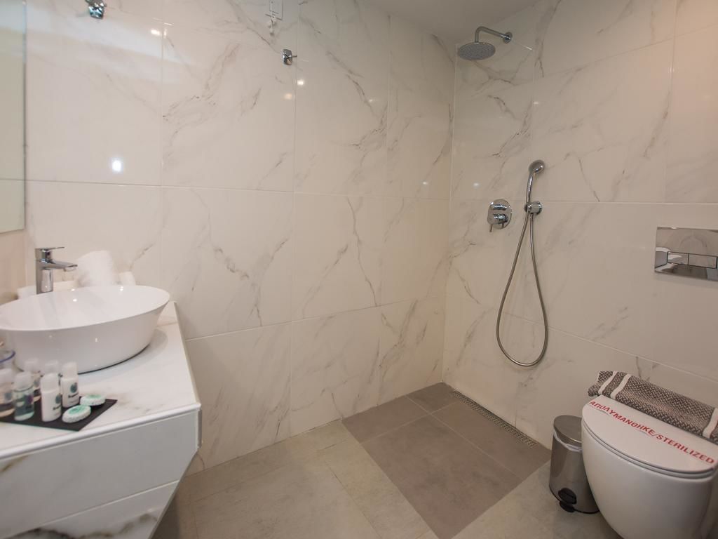Un baño con un lavabo blanco, un espejo, una ducha con cabezal de ducha manual y un inodoro con una toalla.