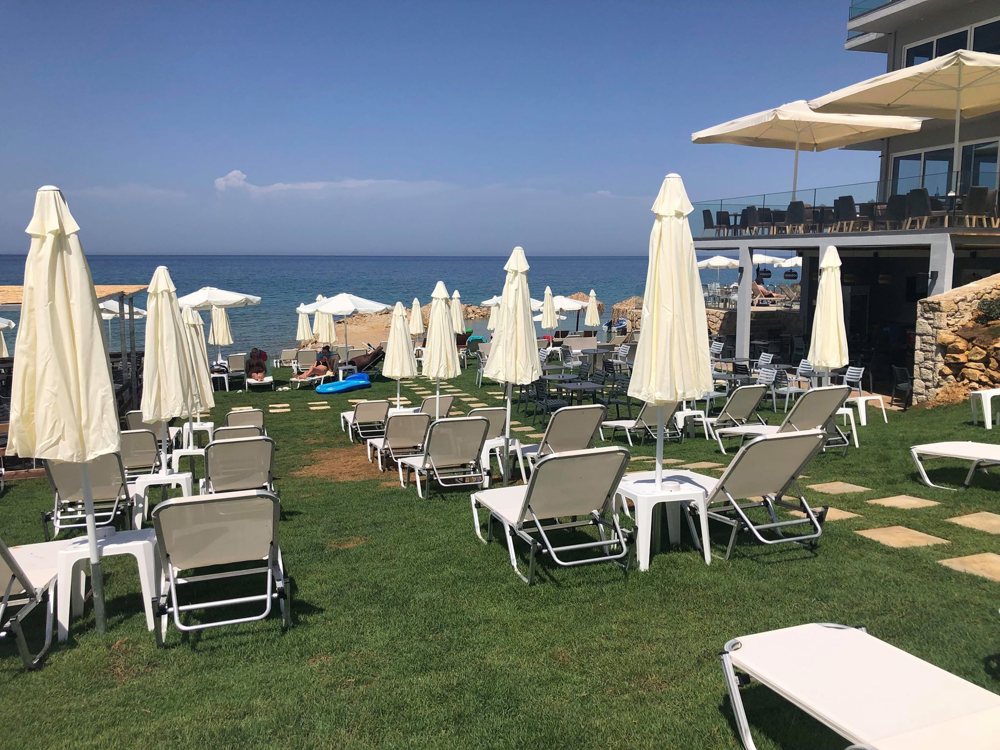A beachside lounge area with white lounge chairs and umbrellas, overlooking the sea.