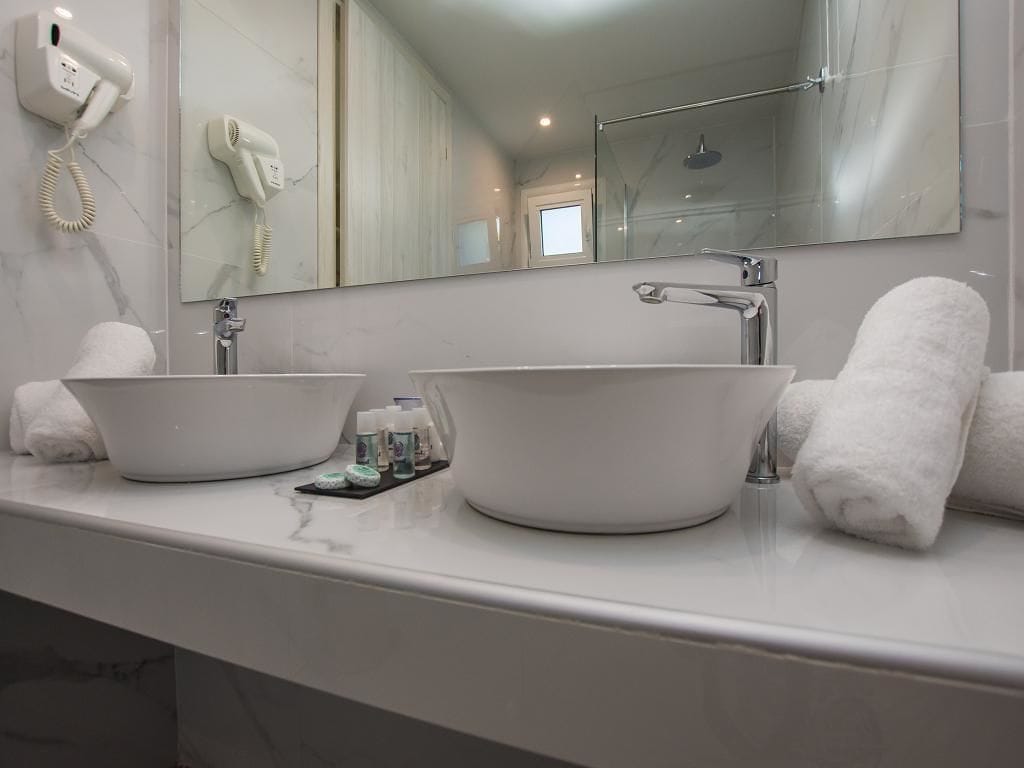 Een badkamer met twee witte wasbakken, een haardroger en een douchecabine van glas.
