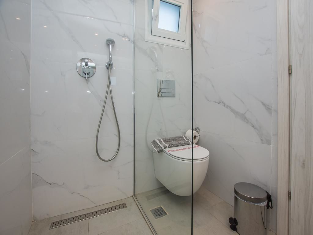 A bathroom with a shower, toilet, and trash bin.
