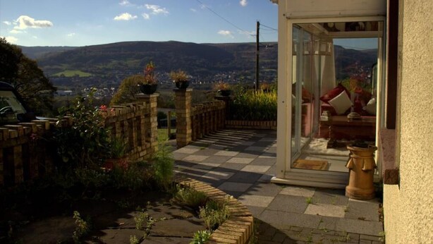 Eine Terrasse mit Schachbrettboden, einer Ziegelwand und Blick ins Tal.