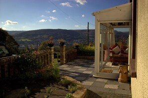 A patio area with a checkered floor, a brick wall, and a view of a valley. - Penybryn Cottages (Aberdare)