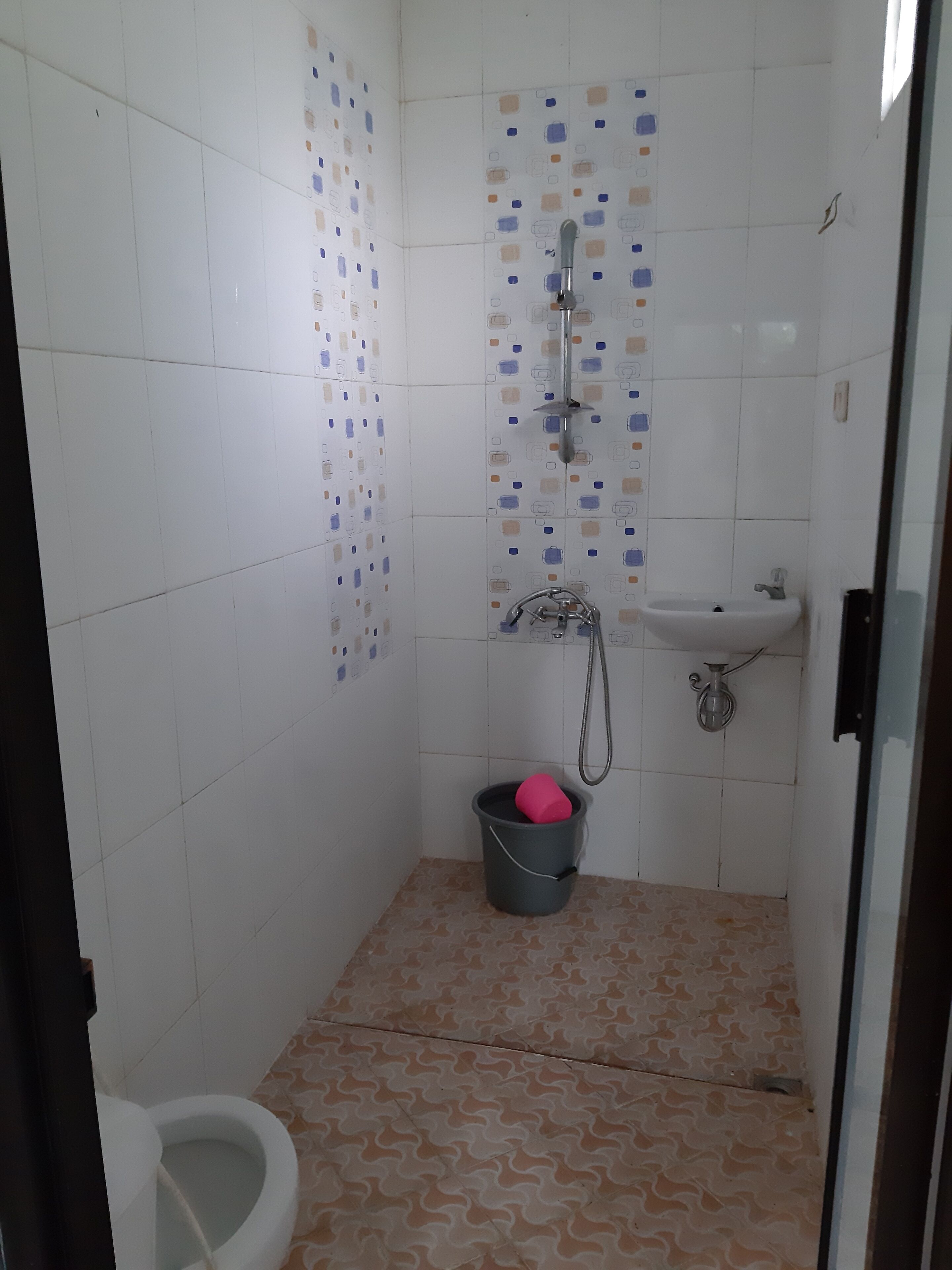 Une petite salle de bain carrelée, équipée de toilettes, d’un lavabo et d’une douche.