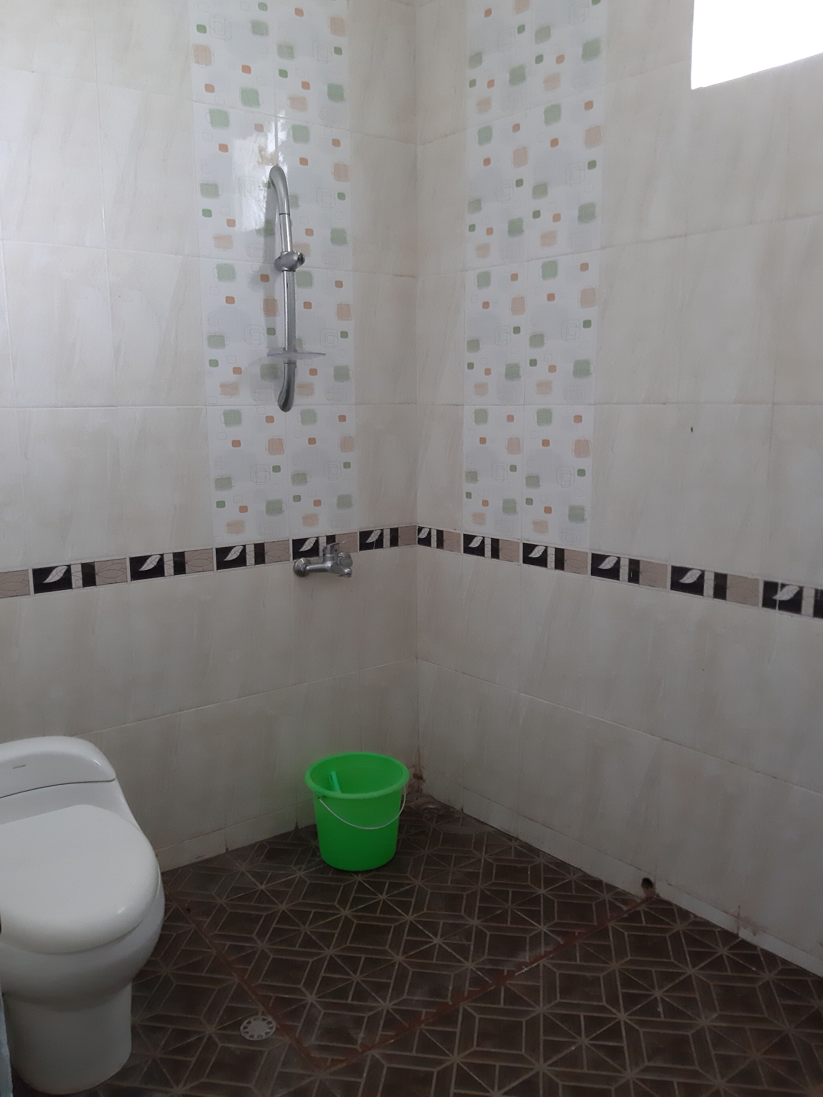 A small bathroom with a toilet, a shower, and a green bucket.