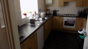 A compact kitchen with wooden cabinets, a built-in oven, a gas stove, and a window with blinds. - A Home From Home 2 (Plymouth)