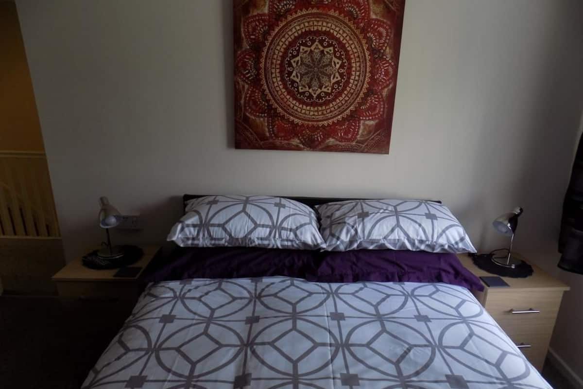 A neatly made bed with patterned bedding, a wall tapestry, and bedside lamps.