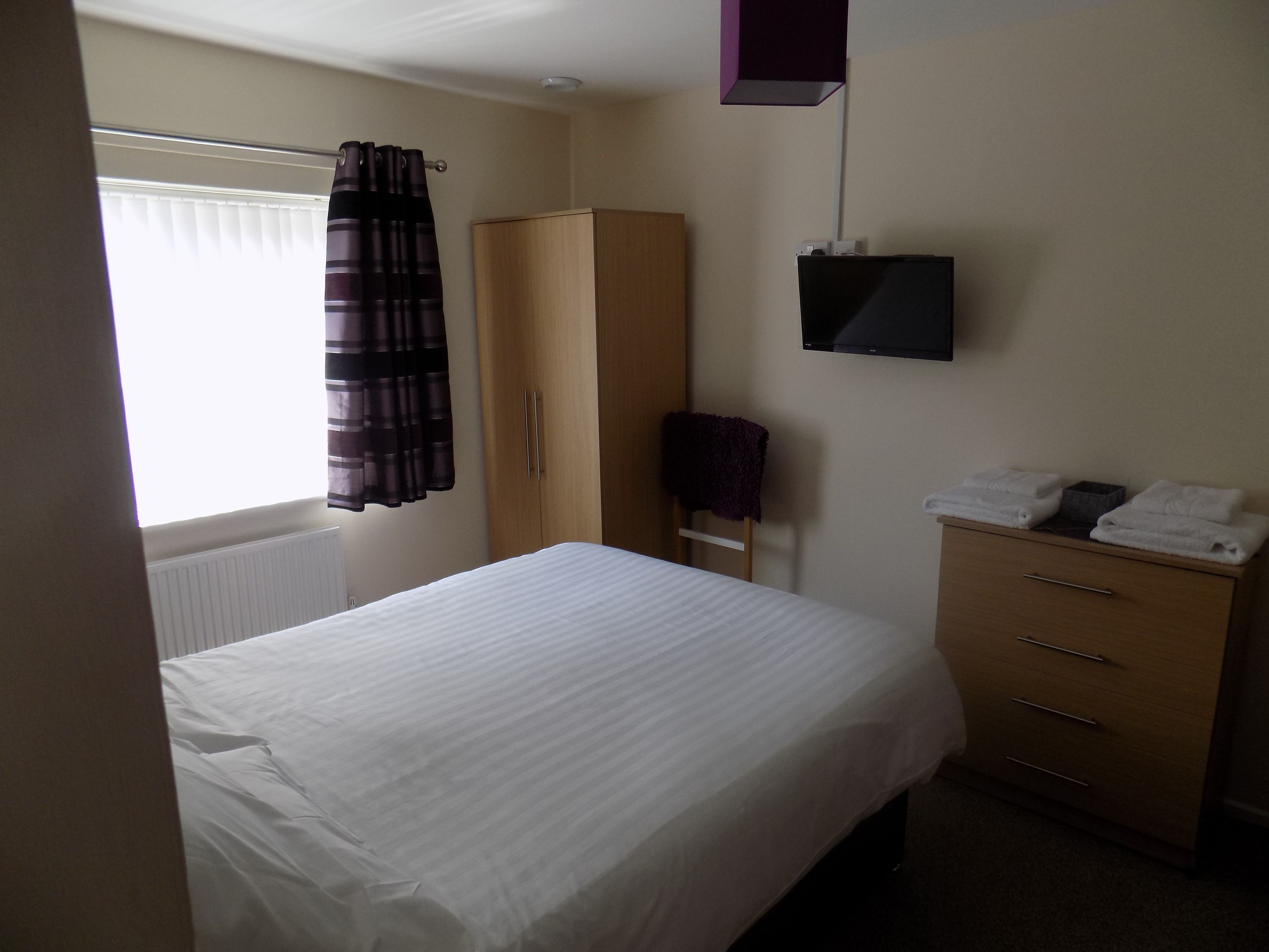 A bedroom with a bed, a wardrobe, a television, and a window with curtains.